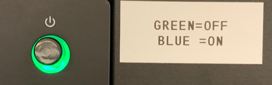 Power button on the left up with a green light on. Sticker on the right that says green equals off and blue equals on.